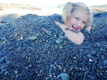 Portrait of cute girl buried in pebbles at beach