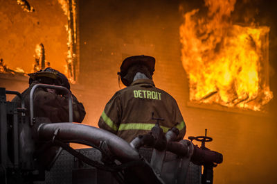 Rear view of firefighters standing against fire