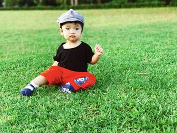 Cute boy sitting on grass in field