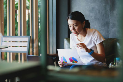 Young woman reading book while sitting on table
