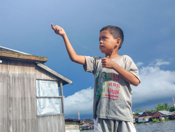 Boy holding string while standing against blue sky