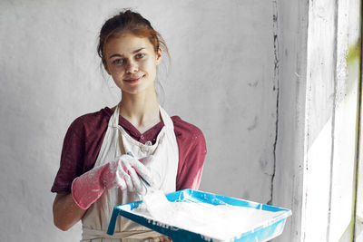 Portrait of young woman holding book while standing against wall