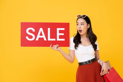 Young woman standing against yellow background