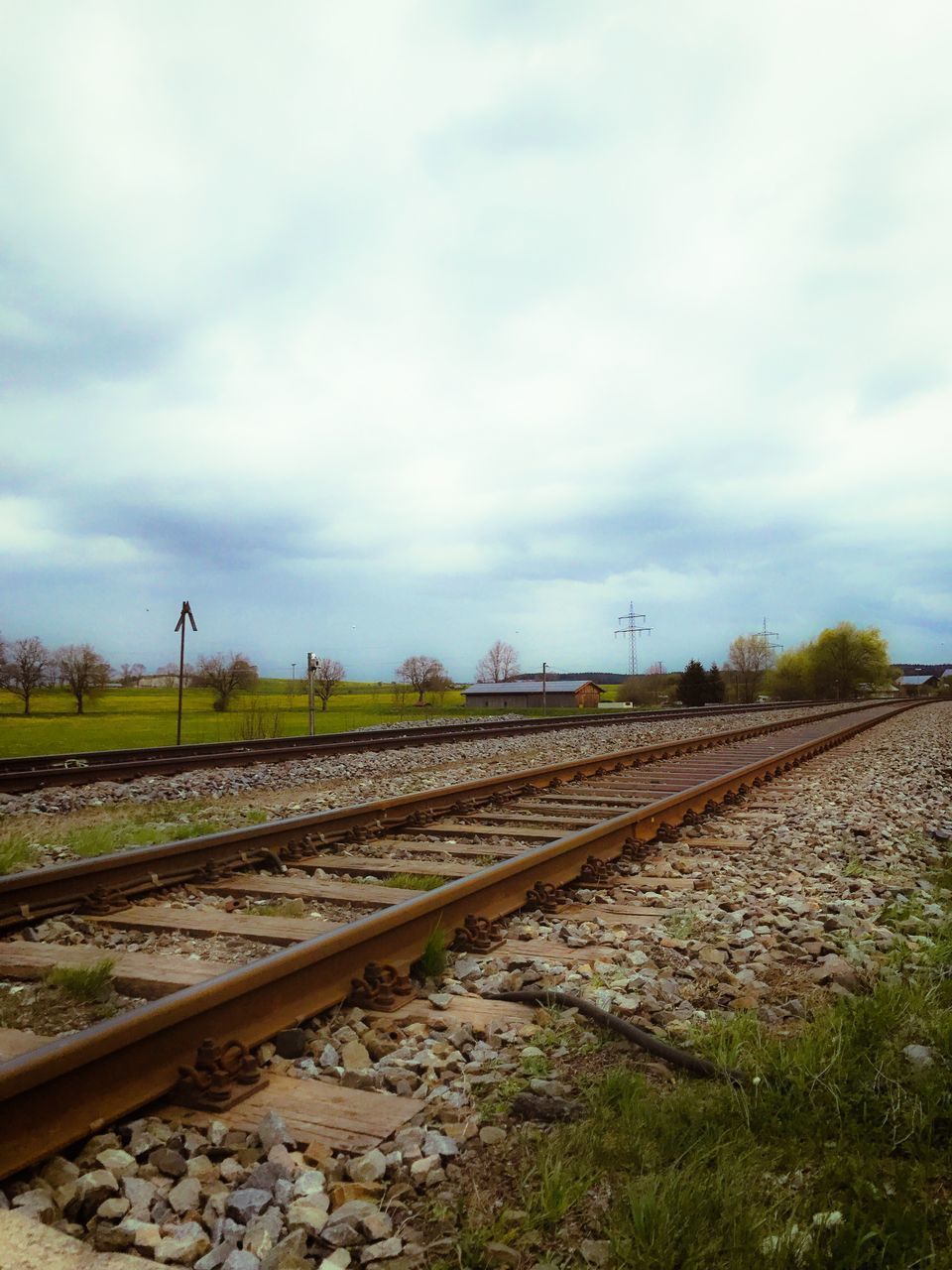 RAILROAD TRACKS BY GRASS AGAINST SKY