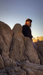 Portrait of boy leaning on rock formation against sky