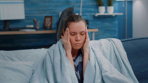 Sick woman with head in hand resting on sofa at home