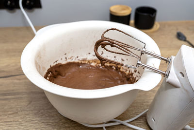 A standing hand mixer with a whisk next to the bowl, with raw dough, the dough is in a thick state.