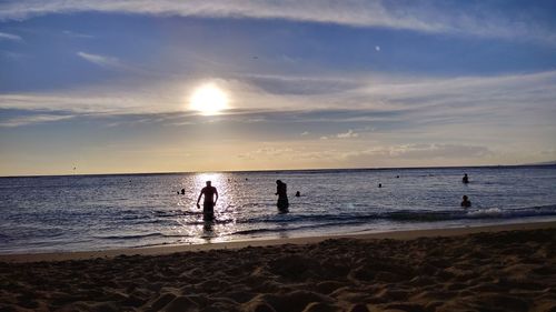 People on beach against sky during sunset