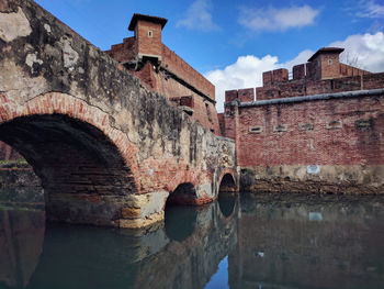 Old bridge over river amidst buildings against sky