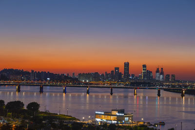 Illuminated city by river against sky at night