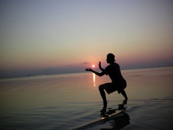 Silhouette man exercising at beach against sky during sunset