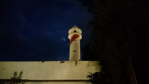 Low angle view of lighthouse by building against sky at dusk