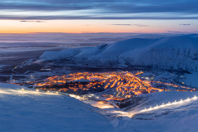 Aerial view of illuminated snowcapped mountains against sky at sunset