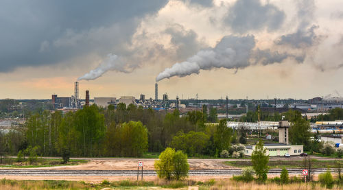 Smoke emitting from factory against cloudy sky