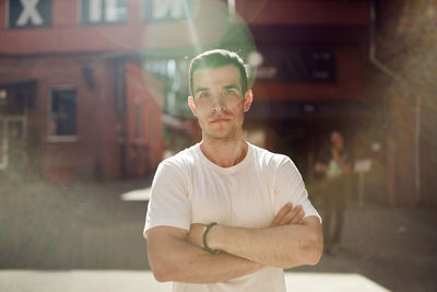 Determined handsome male standing with crossed arms in city street on sunny day and looking at camera