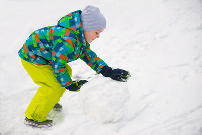 Boy playing with snow while standing outdoors