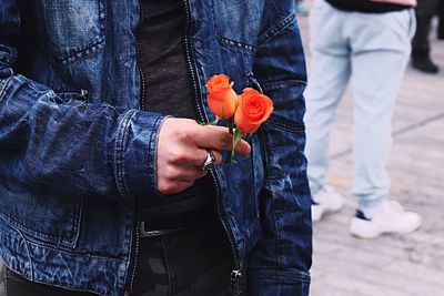 Close-up midsection of man holding roses on street
