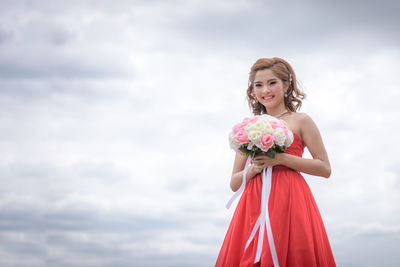 Portrait of a smiling young woman standing against cloudy sky