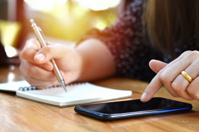 Midsection of woman using mobile phone while sitting on table