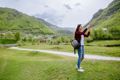 Woman photographing through mobile phone while standing on grassy field