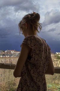 Low angle view of young woman standing against cloudy sky at dusk