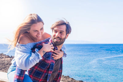 Smiling man piggybacking girlfriend at beach