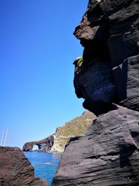 Rock formation by sea against clear blue sky