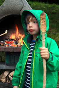 Cute boy holding stick while standing against fire place