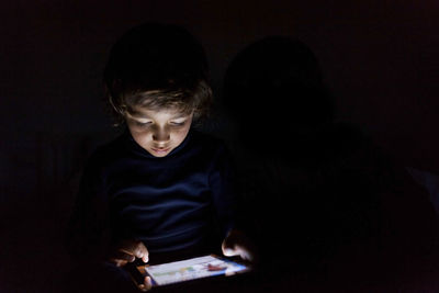 Little boy in darkness playing with digital tablet