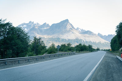 Empty road along trees and mountains against sky