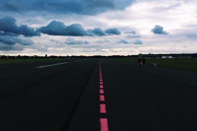 Surface level of empty road on field against cloudy sky
