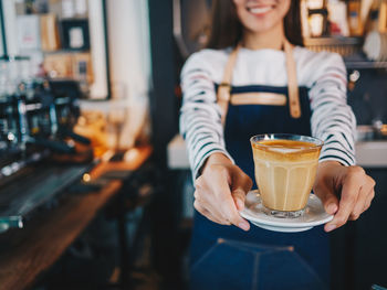 Midsection of woman holding coffee served on table at cafe