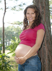 Portrait of a smiling young woman standing on tree trunk