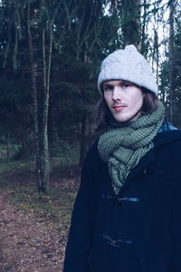 Portrait of young man standing by tree trunk in forest