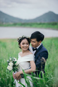 Married couple embracing amidst grass against lake