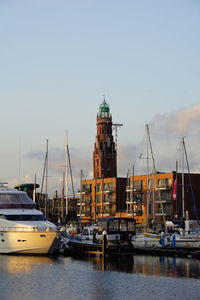 Sailboats moored on harbor by buildings against sky