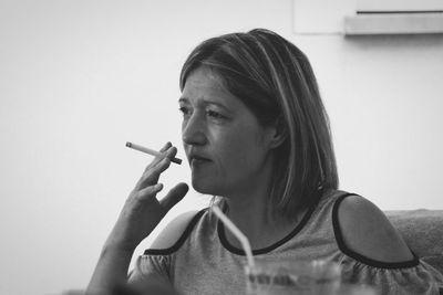 Close-up of mature woman smoking cigarette while sitting on sofa at home