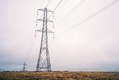 Low angle view of electricity pylon on field against clear sky