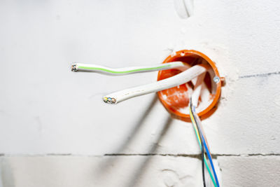 Orange, round junction box mounted in the white wall with protruding electric cables.