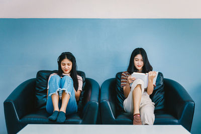 Portrait of smiling young woman sitting on sofa against wall