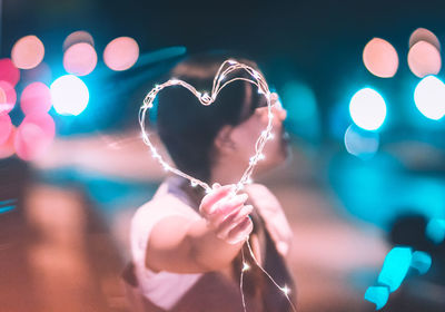 Man holding illuminated heart shape while standing on road at night