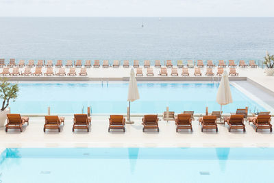 Chairs by swimming pool by sea against sky