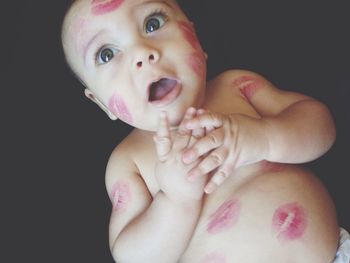 Directly above shot of shirtless baby with lipstick kisses lying against black background