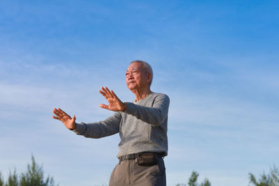 Low section of man with arms raised against blue sky