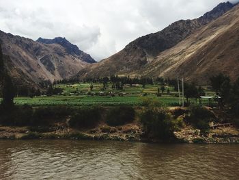 Scenic view of river leading towards mountains against cloudy sky