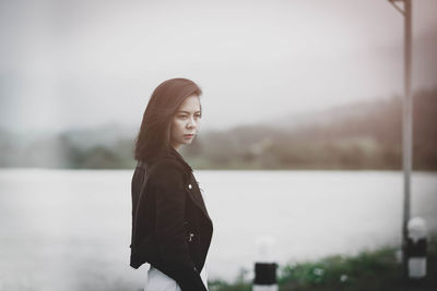 Woman looking away while standing by lake