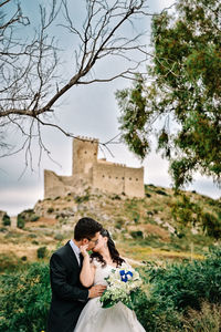 Young couple kissing while standing on mountain against sky