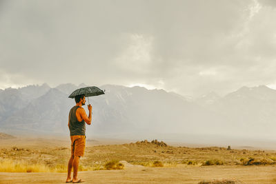 Young man in desert of northern california, holding umbrella in rain.