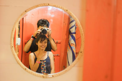 Man and woman with camera reflecting on mirror while photographing