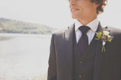 Midsection of smiling bridegroom standing at lakeshore